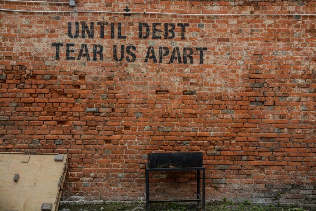 A brick wall with "Until Debt Tear Us Apart" stenciled on the wall