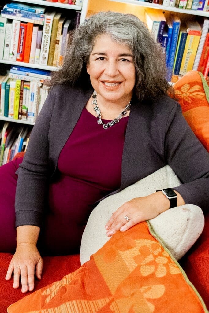 Ida Rose Florez, Ph.D., smiling on a red couch near bookshelves.