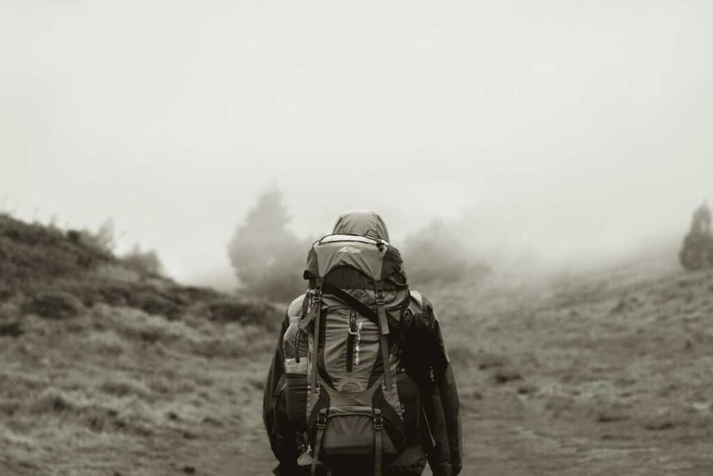 A backpacker hikes up ca hill with a full backpack on a hazy day.