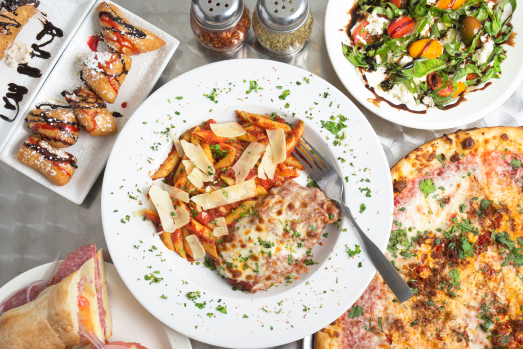 Beautifully garnished assortment of pasta dishes (lasagna, rigatoni, fettuccini pizza, salad, sandwiches and pastries)