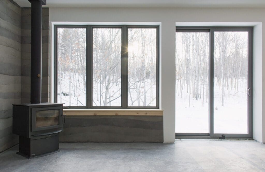 A room with large windows overlooking a snowy landscape, featuring the Interior wood-burning stove on the left side.