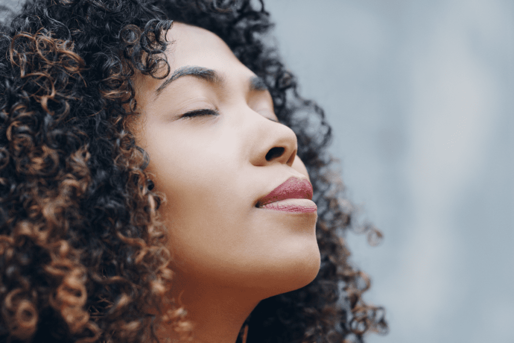A woman takes a deep breath in with her face pointed to the sky.
