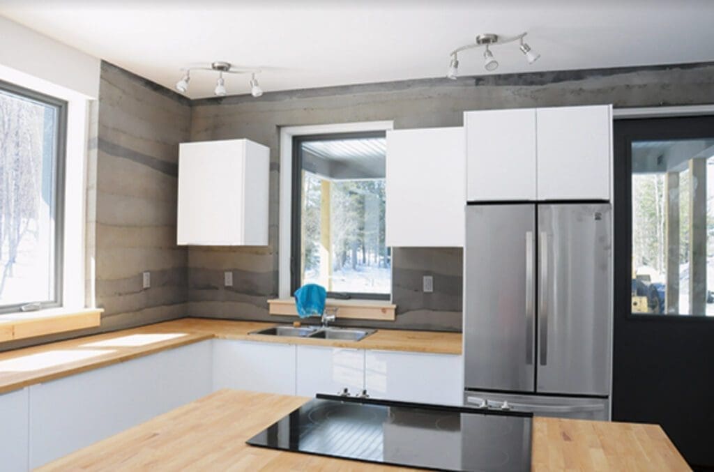 Experience a modern feel with the Kitchen-interior setup featuring light wood countertops, a sleek stainless steel fridge, pristine white cabinets, an electric stove, and large windows that flood the space with natural light.
