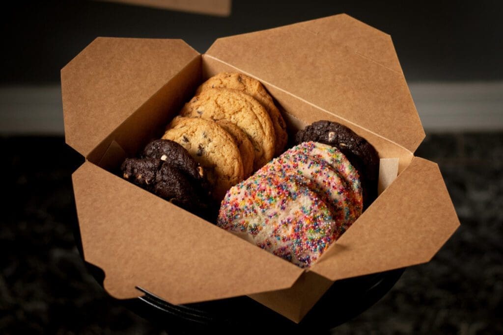 A dozen assorted cookies are lined up in an opened cardboard box.