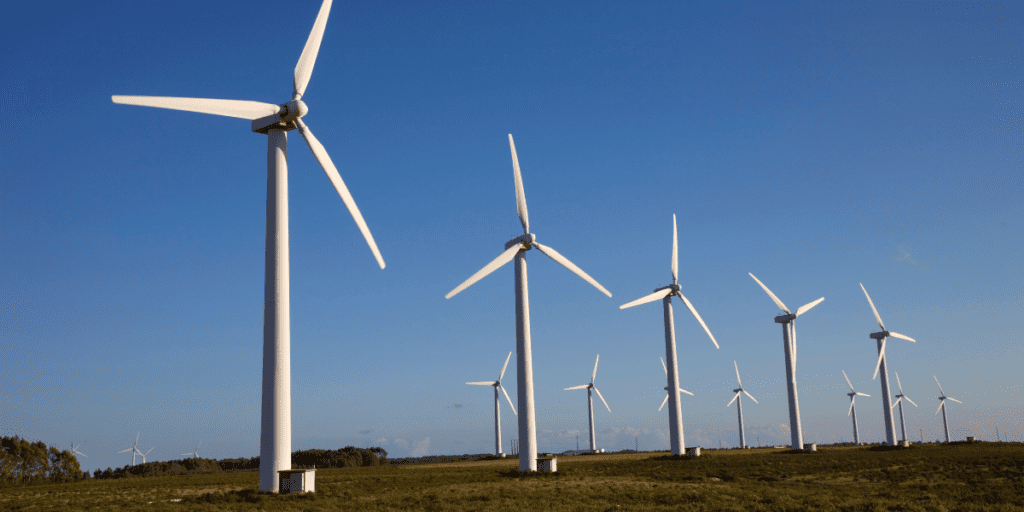 Wind turbines on a grassy plain generate electricity under a clear blue sky.