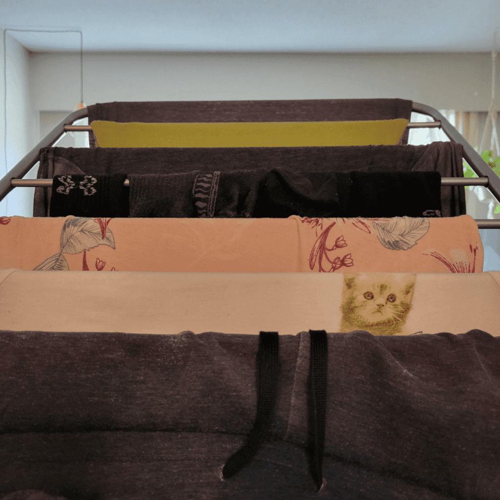 Clothes and a towel with a cat print hang on a drying rack indoors, a small but impactful way to save money and reduce energy consumption.