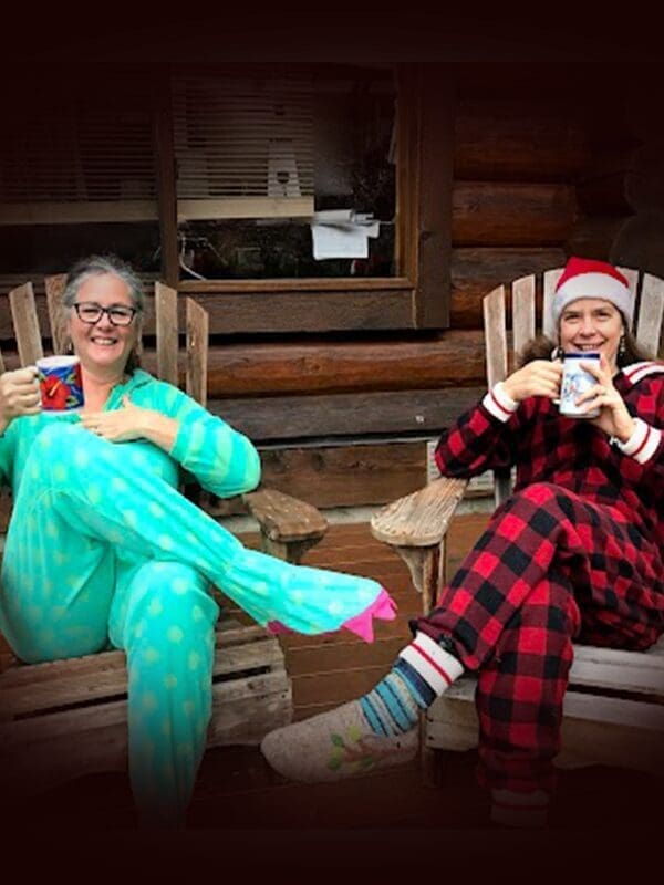 Two people in cozy onesies and slippers sip from mugs on wooden chairs, enjoying a serene moment filled with the warmth of conscious gifting.