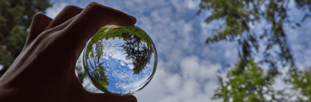 A hand holds a glass sphere reflecting trees, sky, and the LUV Triangle’s inner landscape.