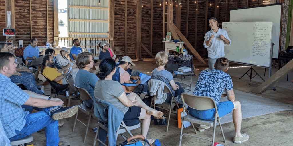 A group maps their inner landscape as a speaker presents by a whiteboard in a rustic setting.