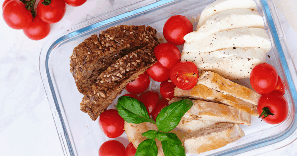 Perfect for outdoors: glass container with sliced bread, tomatoes, mozzarella, and grilled chicken.