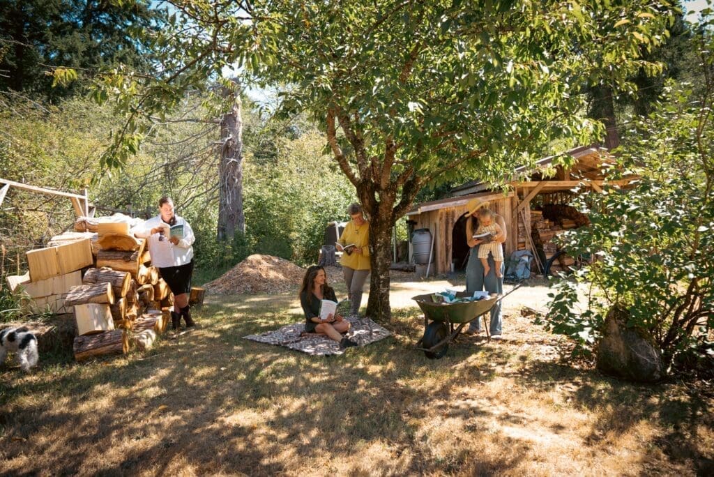 Four people and a dog enjoy a sunny, grassy yard near a rustic shed at this B Corp retreat.