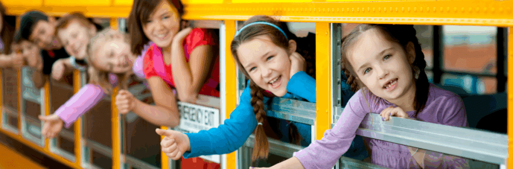 Smiling children lean out of the windows, waving and laughing with summer joy on the school bus.