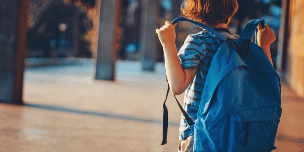 Child wearing a blue backpack walking outdoors, radiating summer joy on a sunny day.