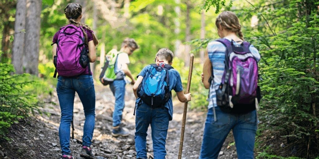 Four kids with backpacks hike a rocky forest trail, savoring the joy of summer adventures.