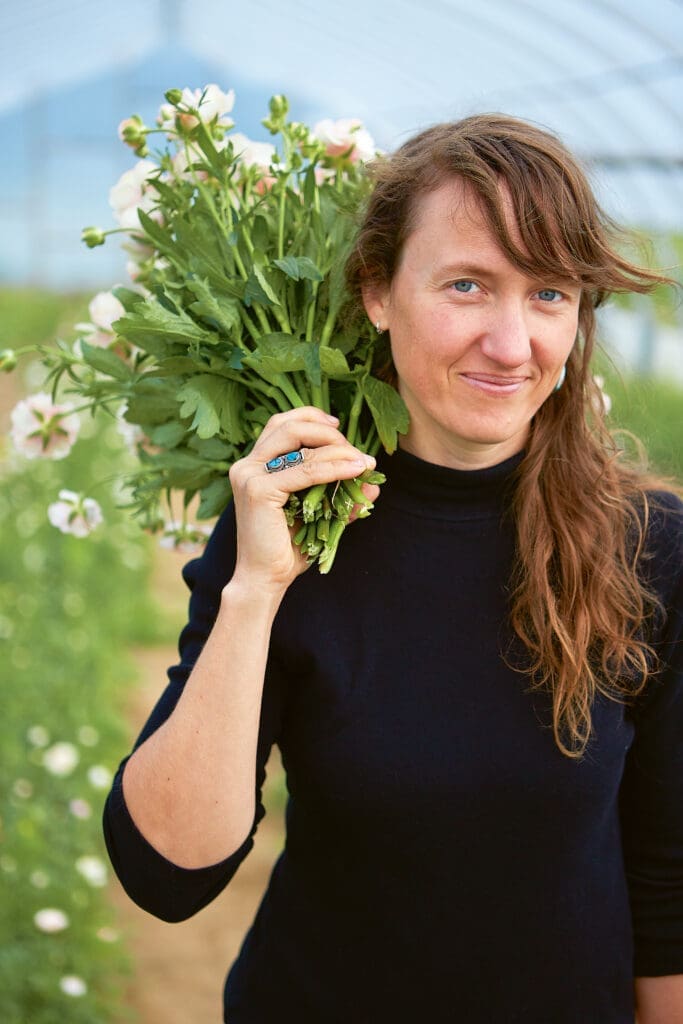 Woman with long brown hair holds a bouquet of flowers on her shoulder in a greenhouse.