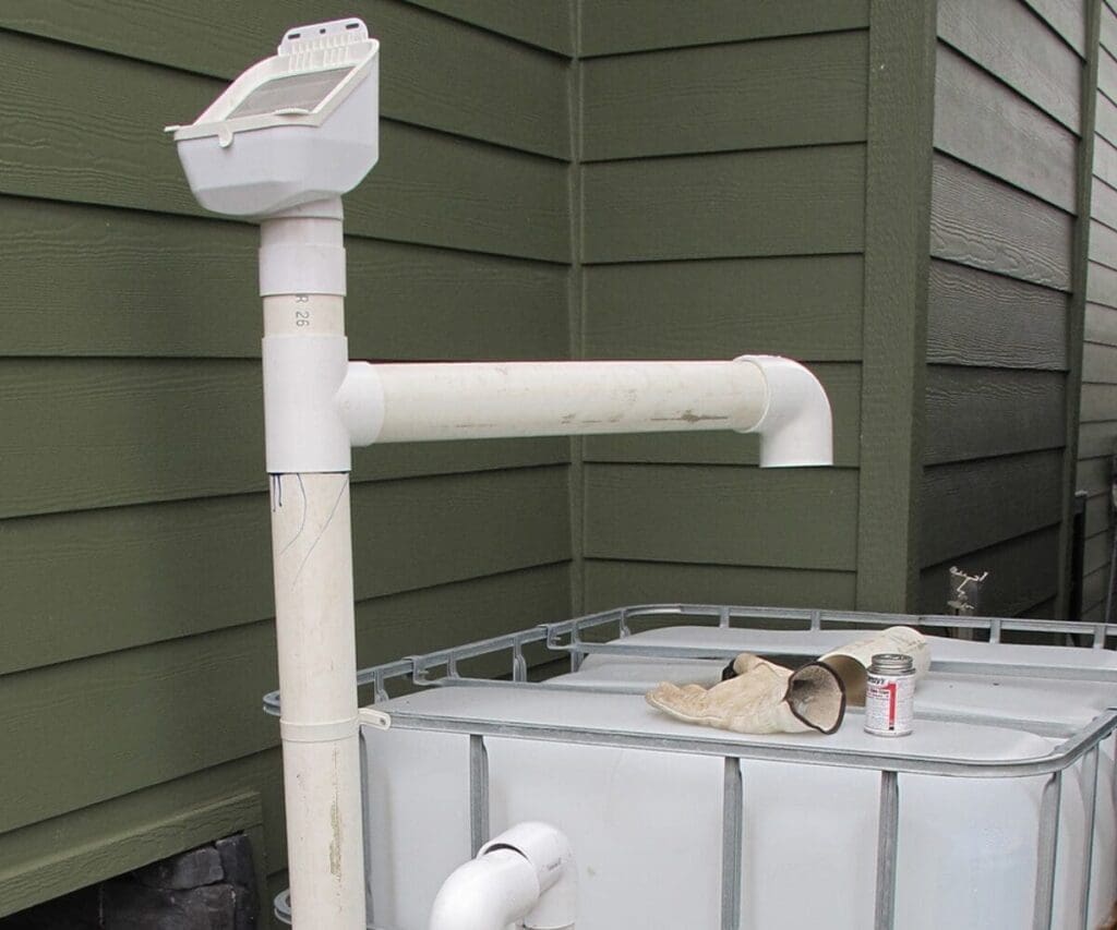 Rainwater harvesting PVC pipe system enhances water security by the green wooden wall and tank.