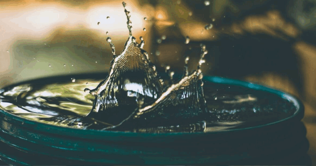 Water splashing up from the surface of a dark container in mid-air.
