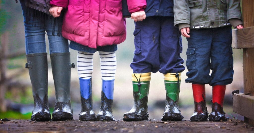 Four children in colorful rain boots talk to kids about climate change outdoors in 2025.