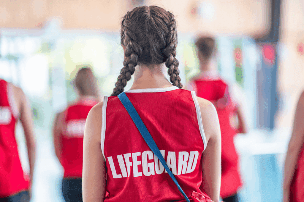 Person with braids in a red "Lifeguard" shirt, embodying thriving youth, seen from behind indoors.