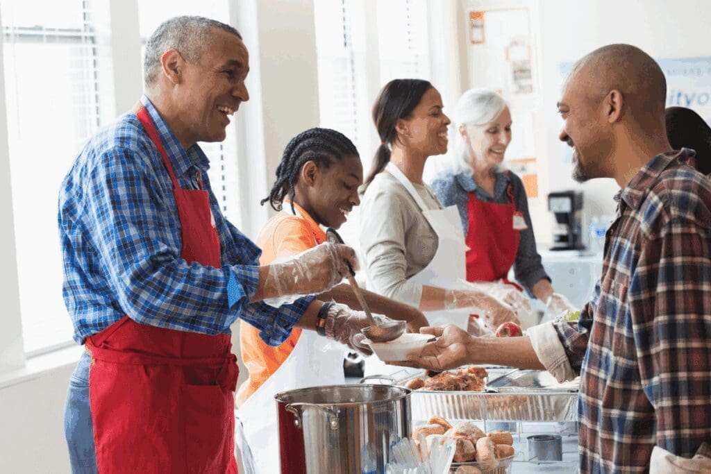 Volunteers in red aprons serve food, sharing meaningful gifts at a festive community kitchen.