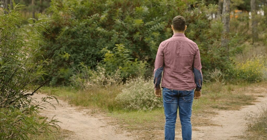 Man in jeans stands at a fork, choosing a path toward action for a better world.