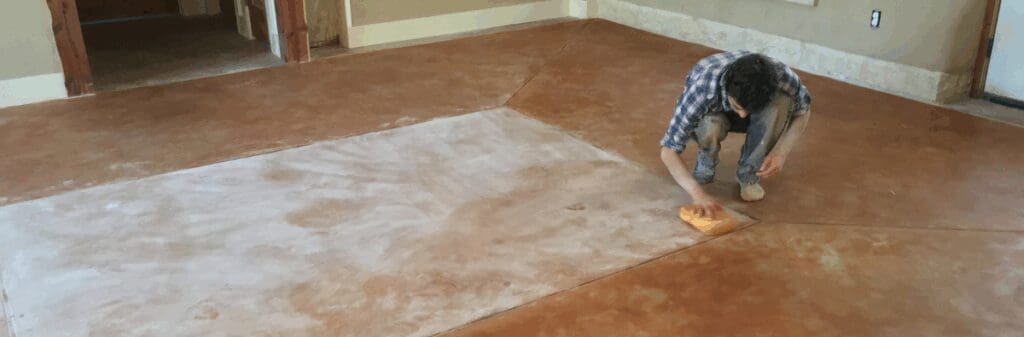 James Thomson kneeling and cleaning stained earthen floors with a sponge.
