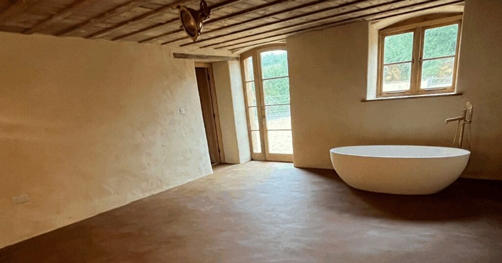 Minimalist bathroom with freestanding bathtub, rustic ceiling, and earthen floors.