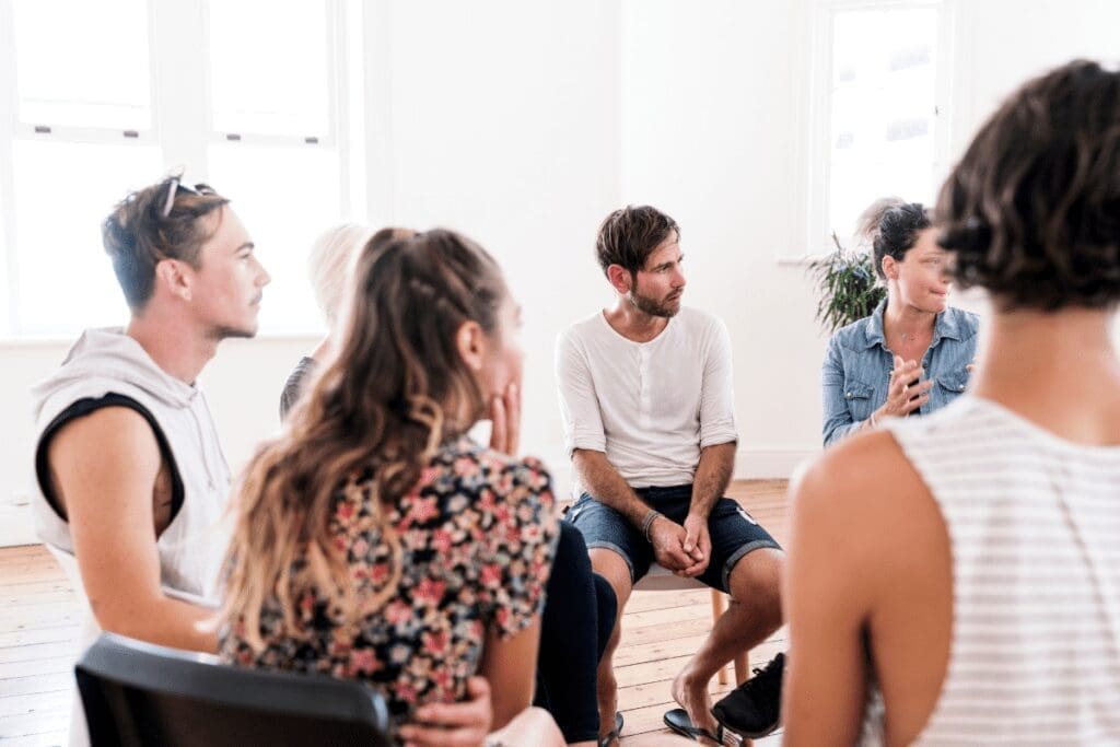 A group discusses Collective Liberation in a bright room with wooden floors.