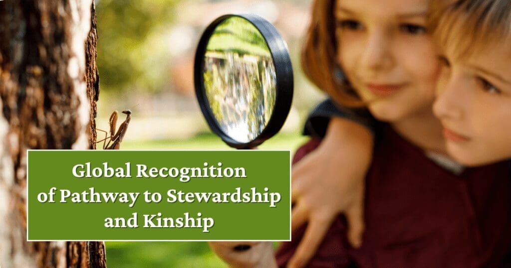 Two children use a magnifying glass to observe a praying mantis, sparking stewardship.