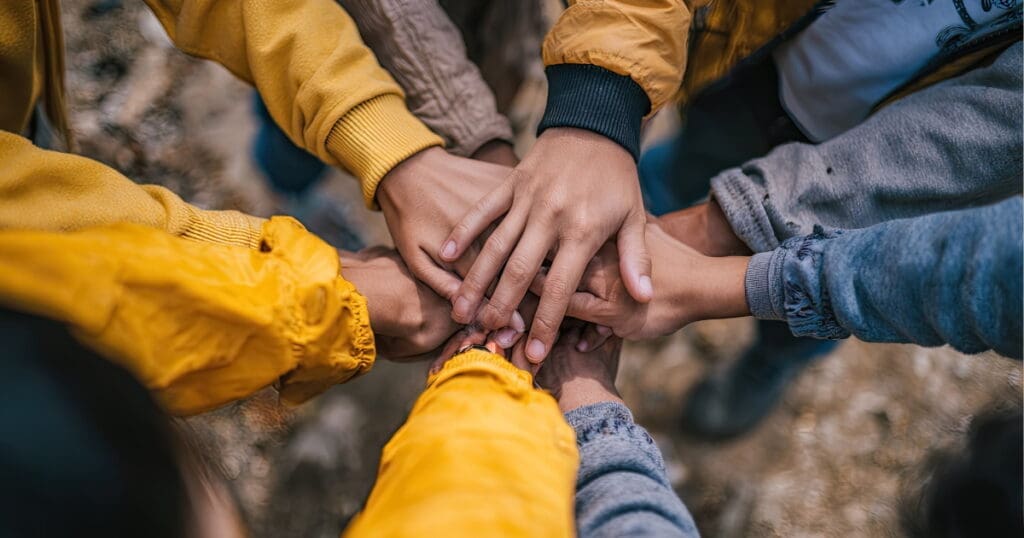 A group of people stacking their hands, symbolizing unity and the spirit of Collective Liberation.
