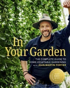 Smiling man in a hat stands in garden with the book "In Your Garden.