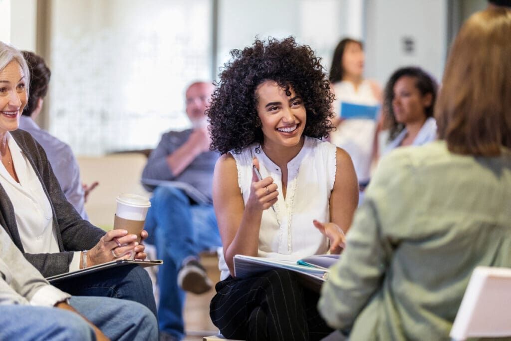 Woman smiles and gestures while facilitating a meaningful workshop in a bright, casual setting.