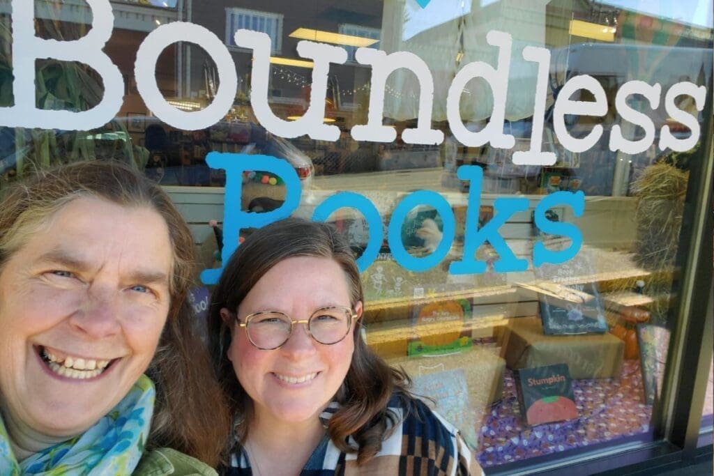 Two smiling women outside Boundless Books, a community-focused independent bookstore.