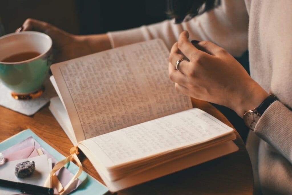 Workshop facilitator holding tea and reading a handwritten journal at a wooden table.