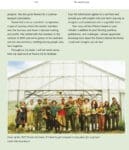 A group of people stand smiling together inside a greenhouse with plants and farming tools.