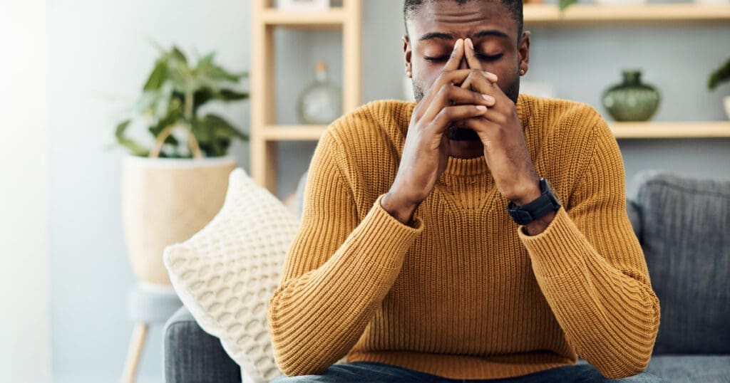 Man in yellow sweater shows burnout, eyes closed and fingers pressed to forehead in stress.