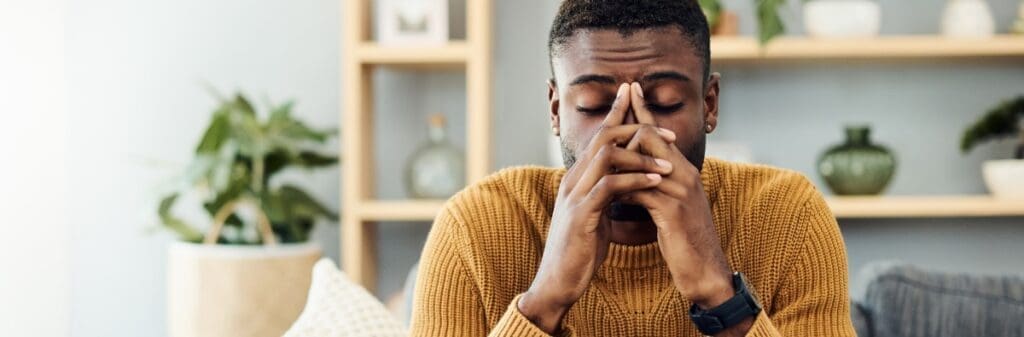 Man in yellow sweater sits with eyes closed, showing signs of work stress or burnout.