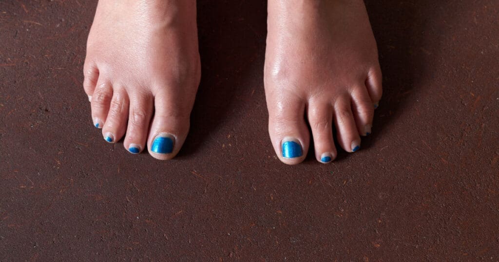 Two bare feet with blue toenail polish standing on an earthen floor.