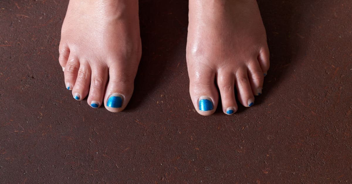 Two bare feet with blue toenail polish standing on an earthen floor.