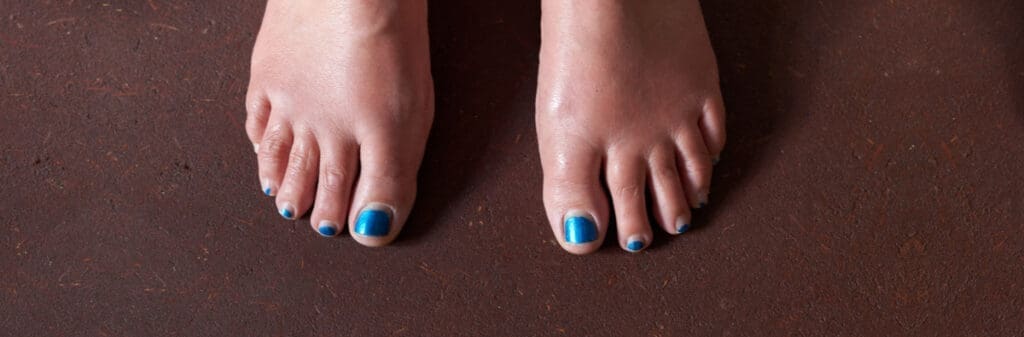 Two feet with blue toenails standing on an earthen floor, perfect for summertime vibes.