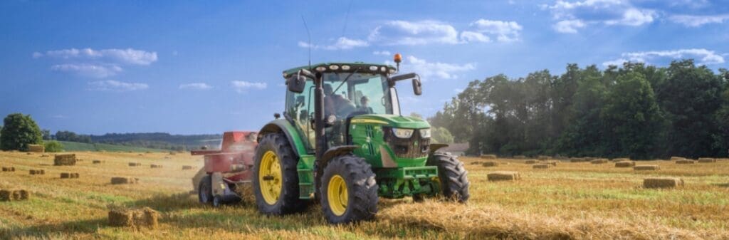 Green tractor baling hay in a sunny field, showcasing sustainable agriculture under blue skies.